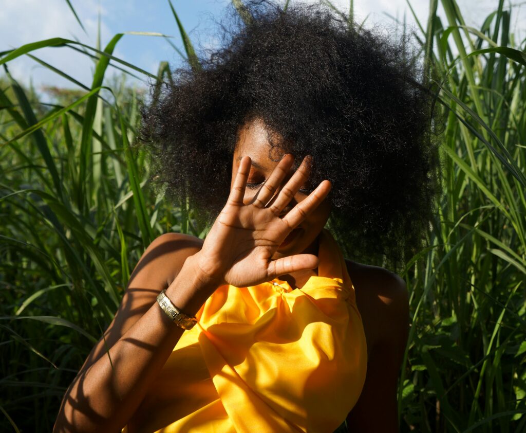 Beautiful woman with natural hair sitting in lush greenery, enjoying a peaceful moment.